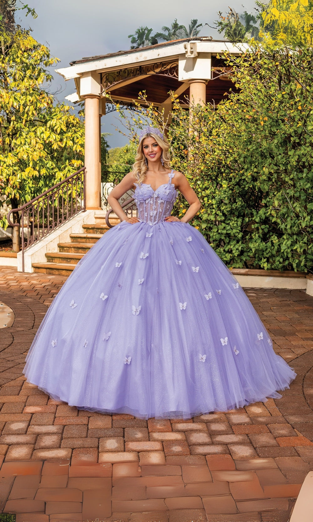 Woman in a lavender ball gown standing outdoors on a brick patio with greenery.