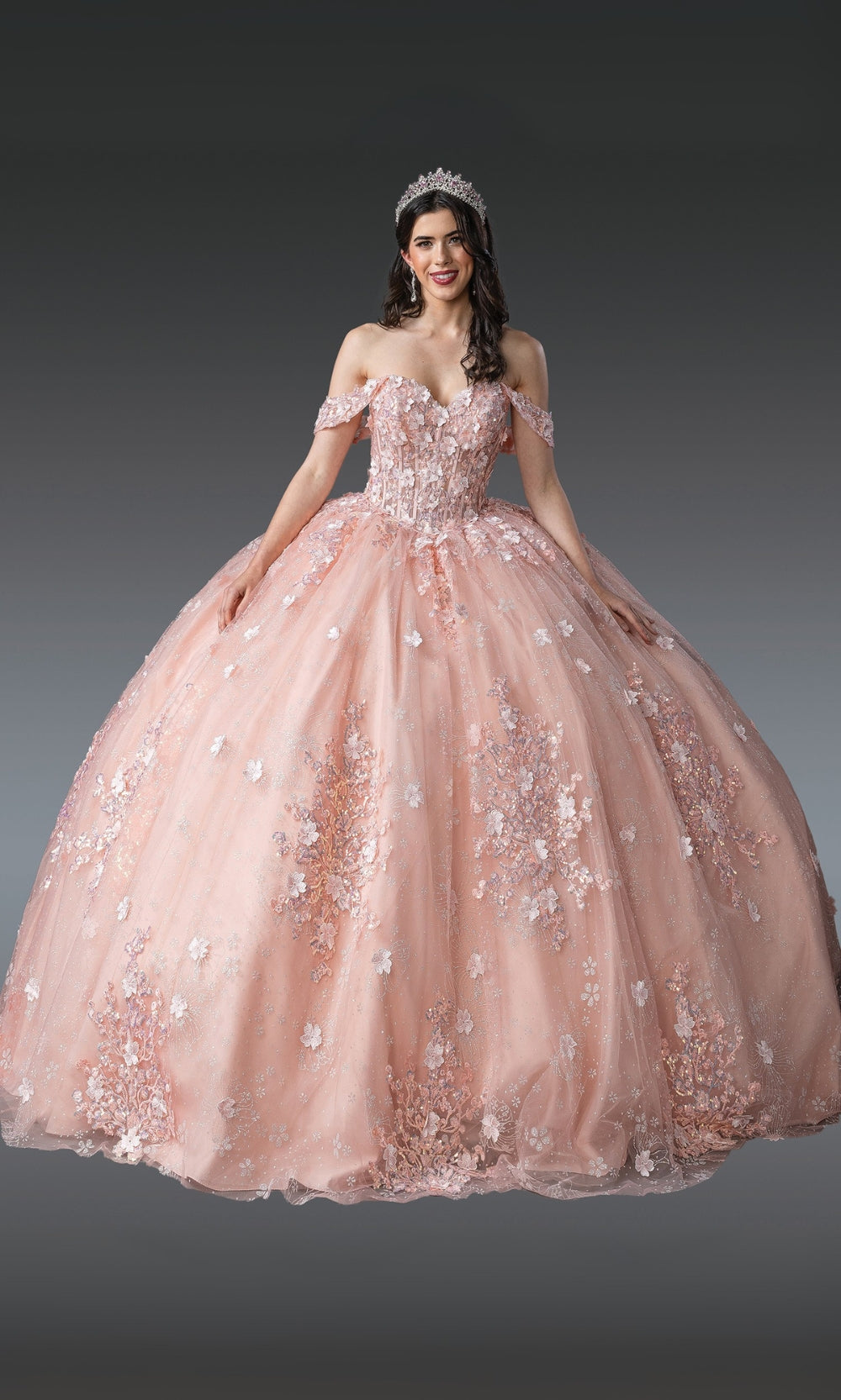 Woman wearing a pink ball gown with floral embellishments on a gray background