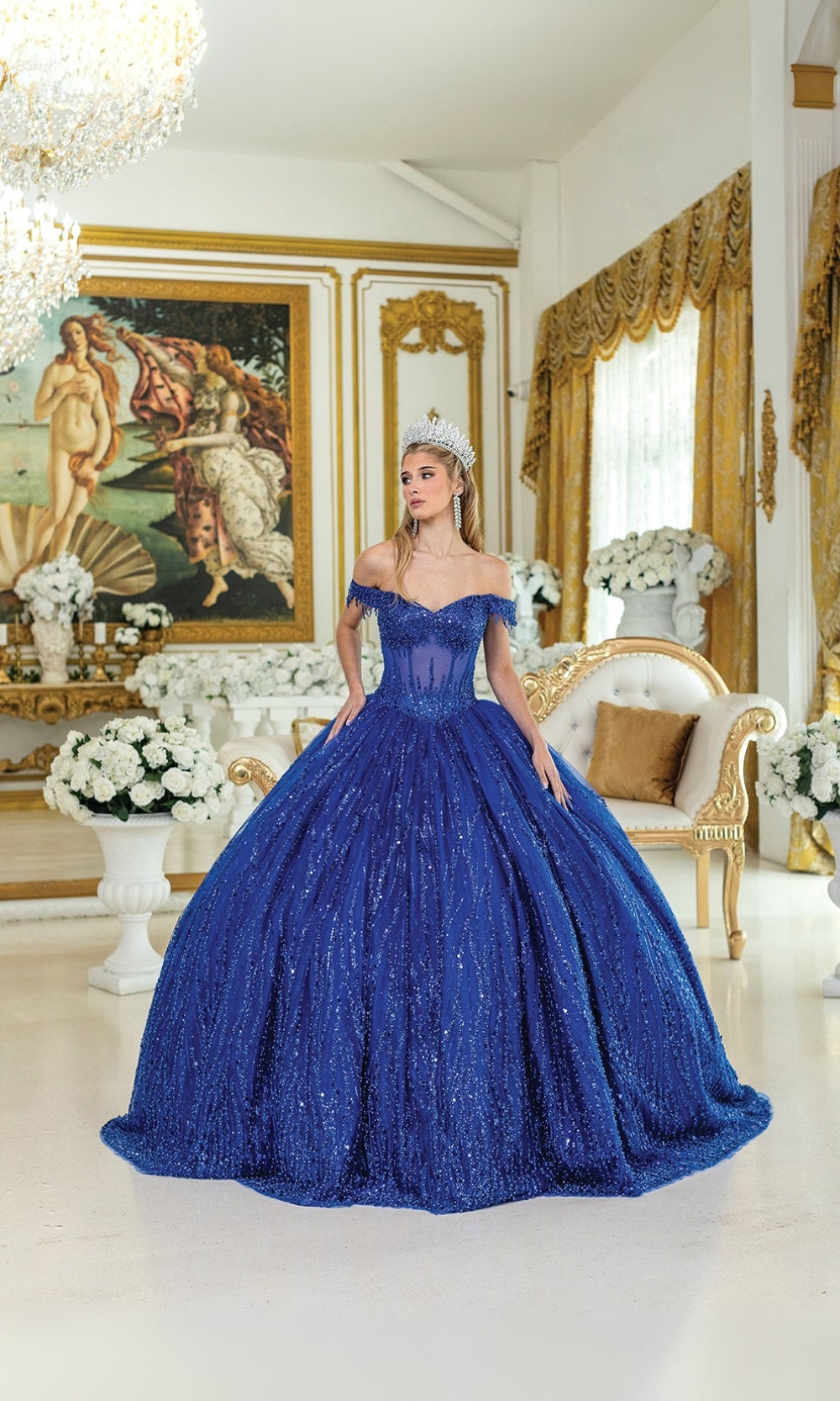 Woman in a blue off-shoulder gown standing in an ornate room with classical art and decor.