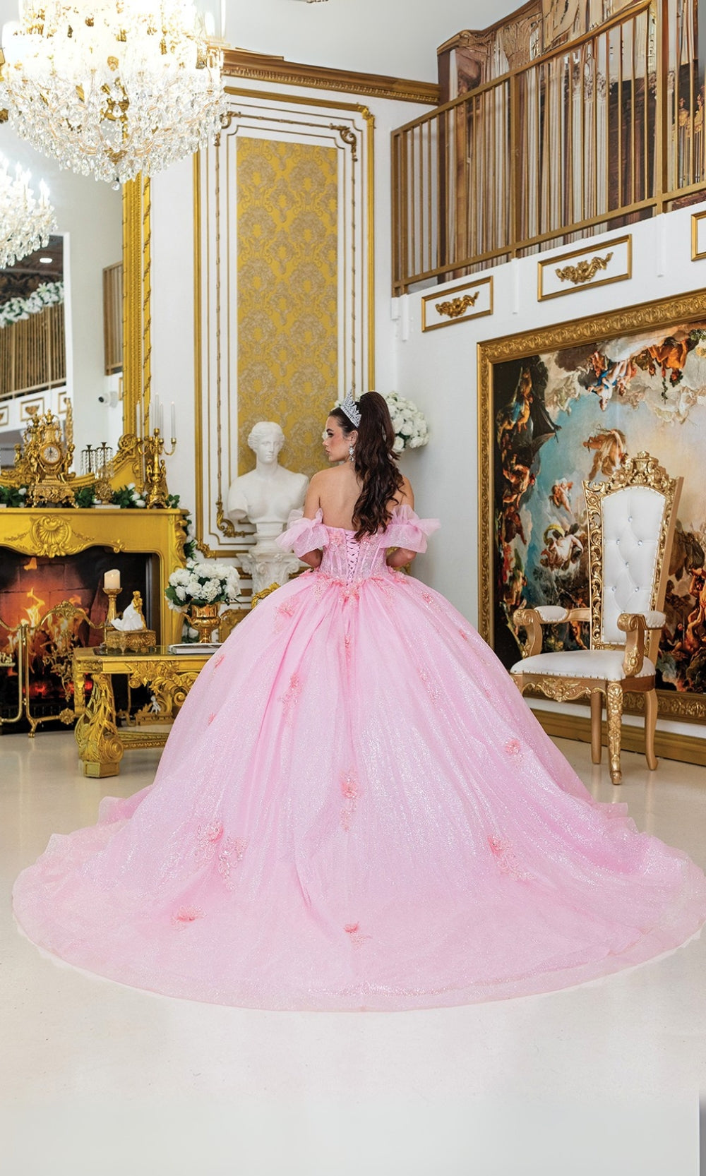 Woman in a pink ball gown standing in an opulent room with gold decor and artwork.