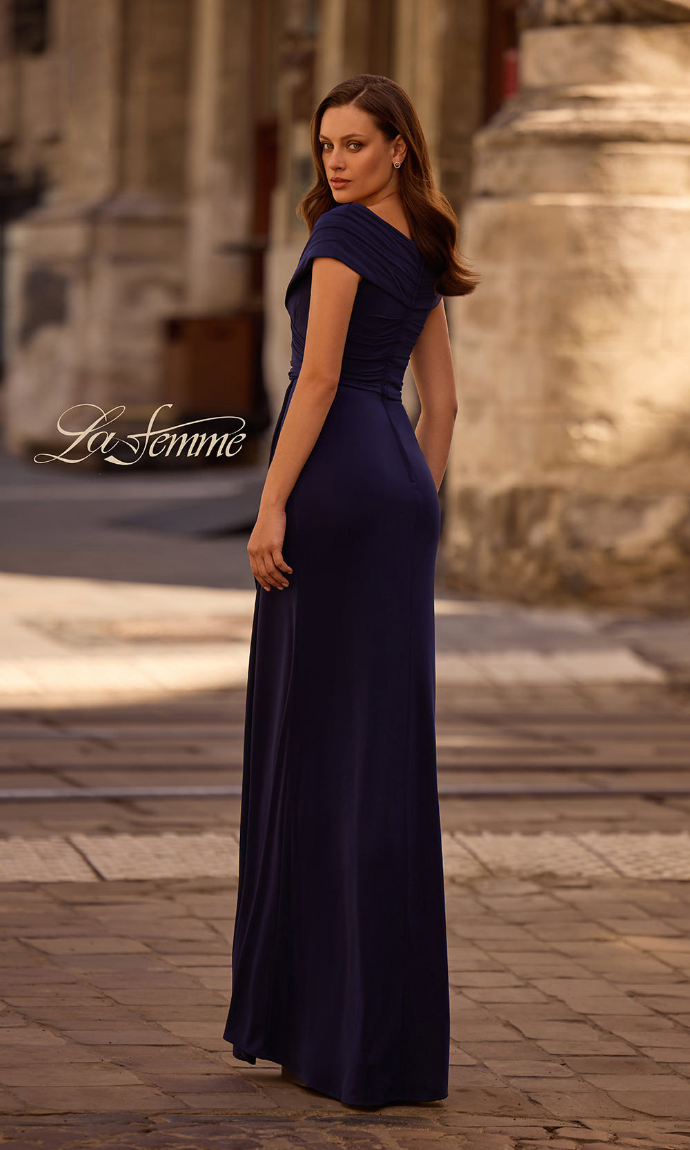 Woman wearing a navy blue evening gown in an outdoor setting with 'La Femme' branding.