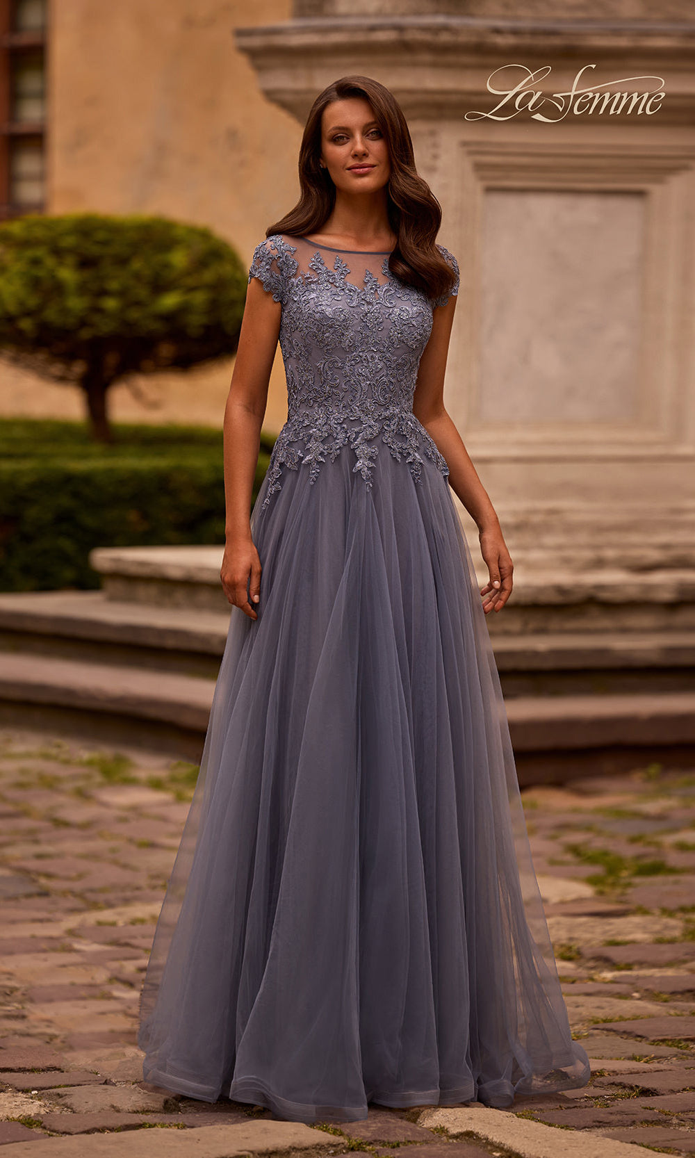 Woman in a gray evening gown standing outdoors with classical architecture in the background