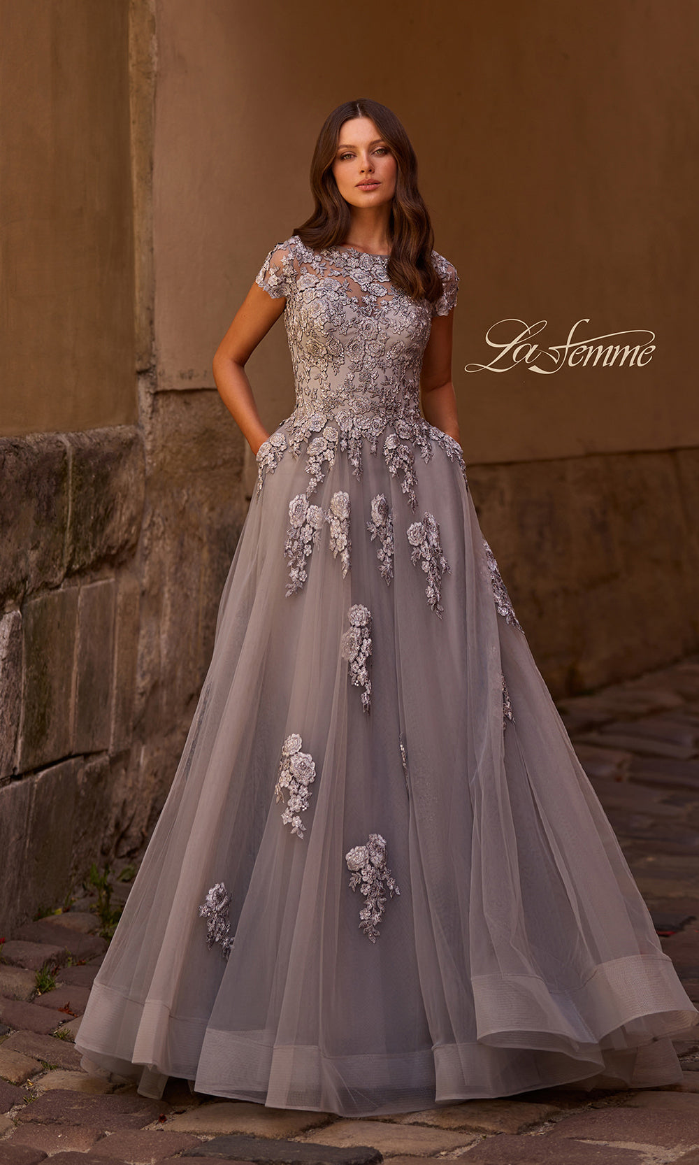 Woman wearing a gray evening gown with floral embellishments in an outdoor setting.