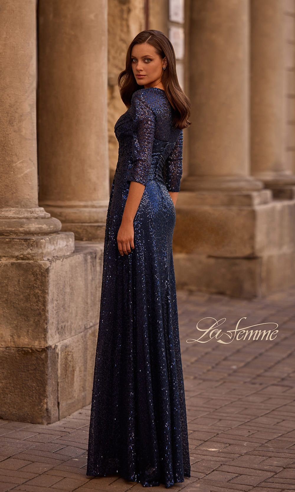 Woman in a long, dark blue evening gown standing in front of stone columns.