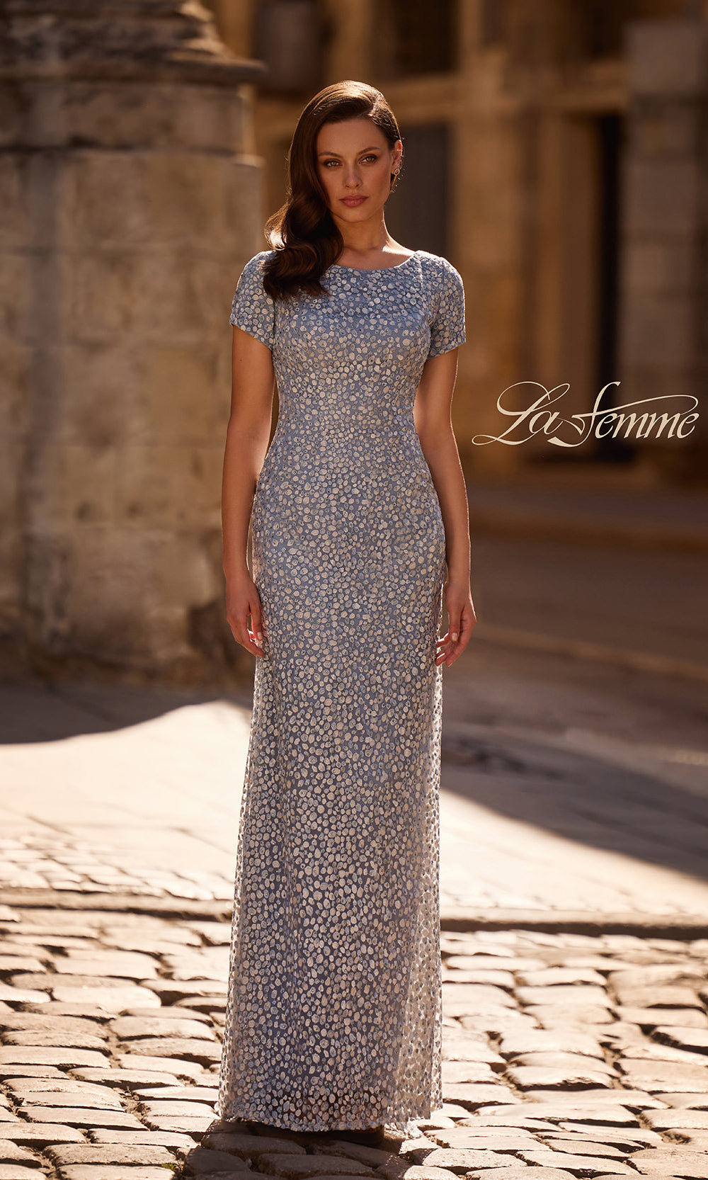 Woman in a long, patterned dress standing on a cobblestone street with 'La Femme' branding.