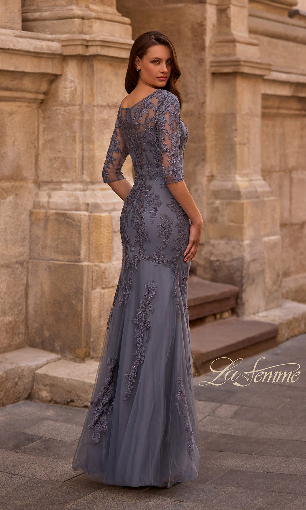 Woman wearing a gray lace evening gown in front of stone architectural background