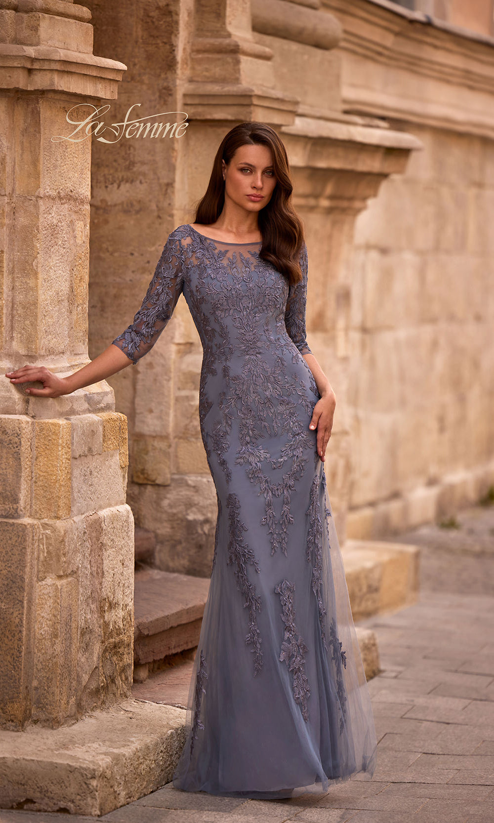 Woman in a blue evening gown standing against a stone wall.