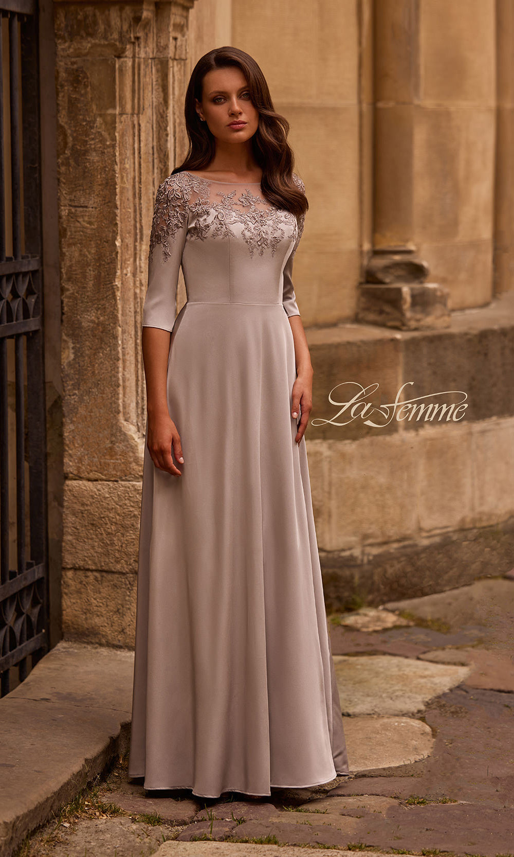 Woman wearing a elegant dress with lace detailing in front of a stone building.