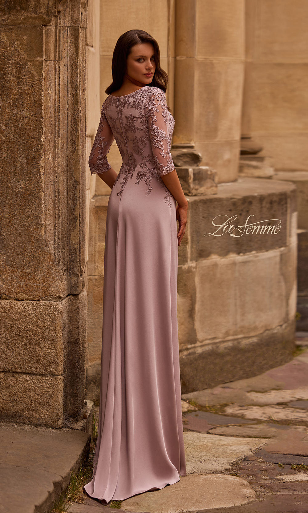 Woman in a long, elegant dress standing against a stone wall.