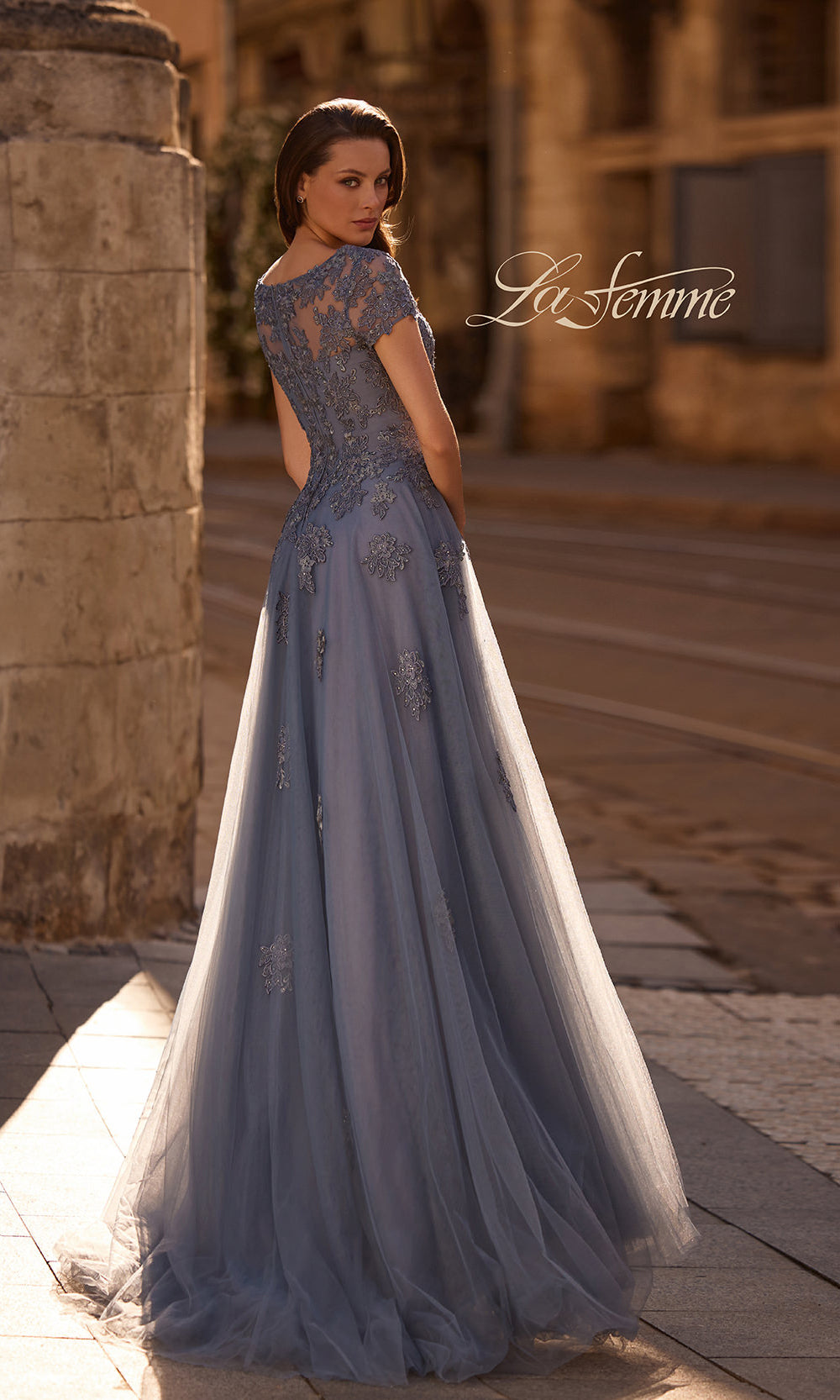 Woman wearing a blue evening gown with lace details on a stone path.