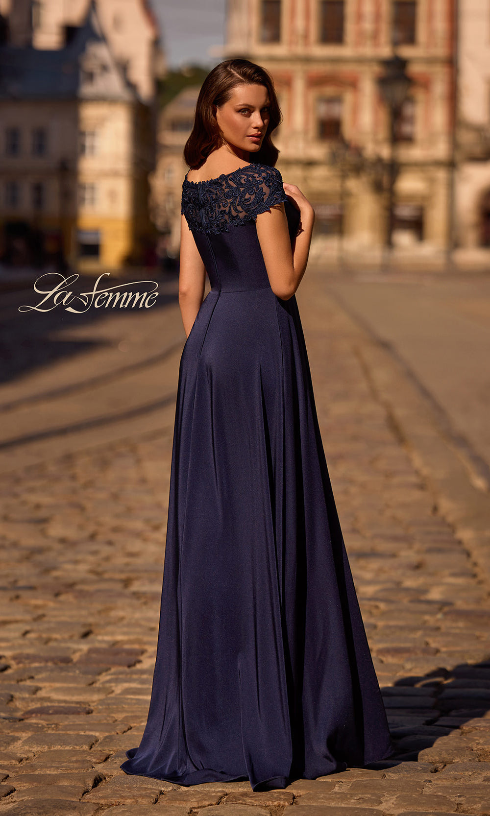 Woman in a long navy blue evening gown with lace top on a cobblestone street.