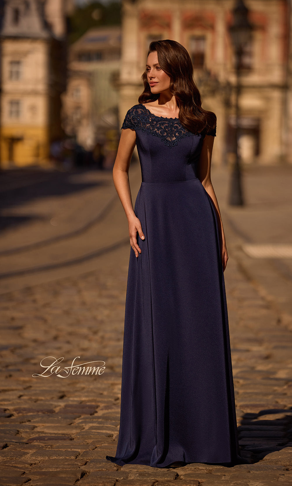 Woman in a long dark blue dress standing on a street with blurred background