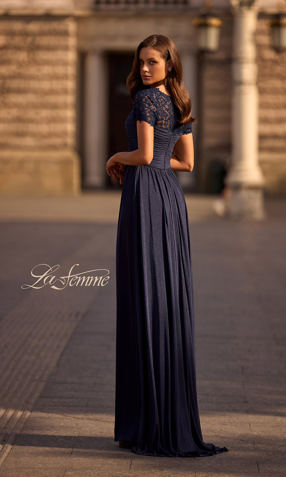 Woman wearing a long dark blue dress with lace details in an outdoor setting.