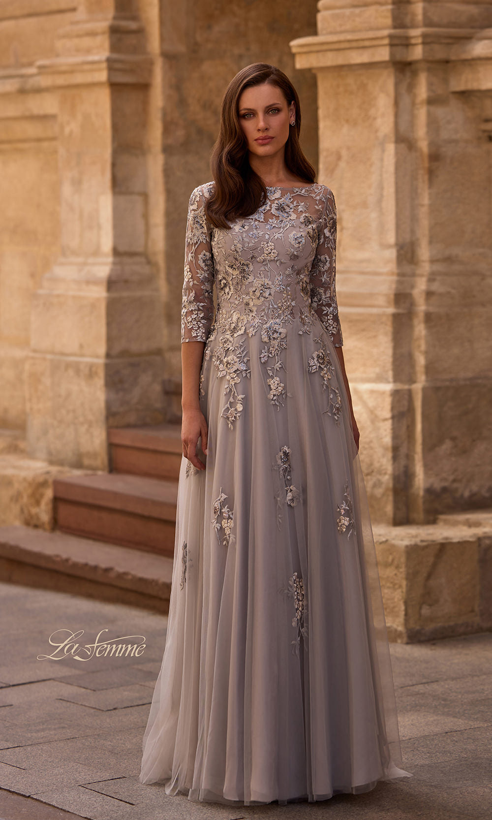 Woman in a long, elegant dress standing in front of a stone building.