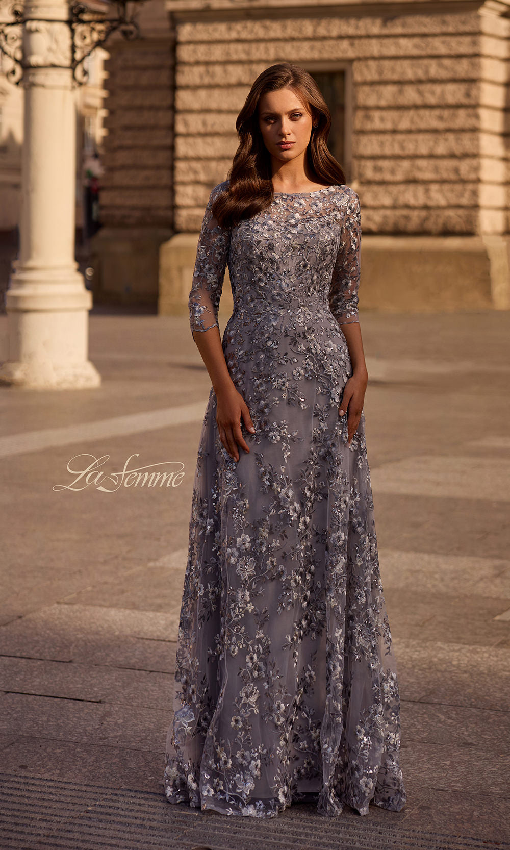 Woman wearing a floral evening gown in an outdoor setting with 'La Femme' branding.