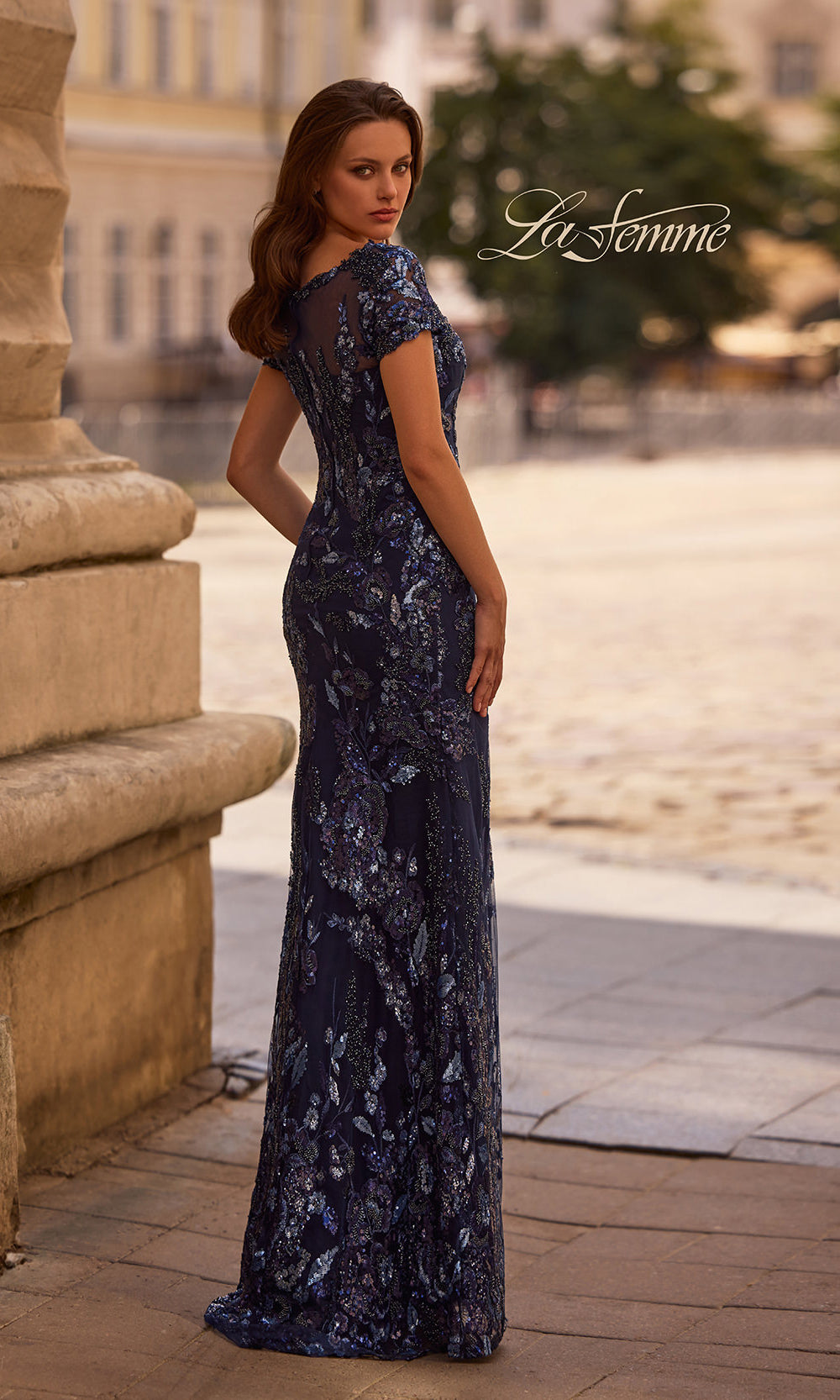 Woman wearing a dark blue evening gown with floral patterns in an outdoor setting.