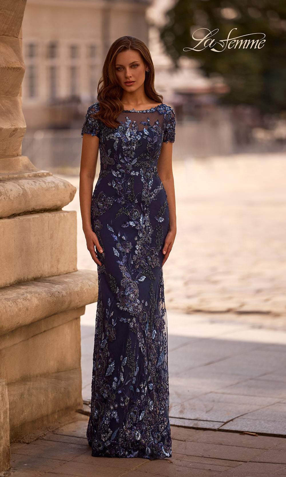 Woman wearing a dark blue lace evening gown standing outdoors.