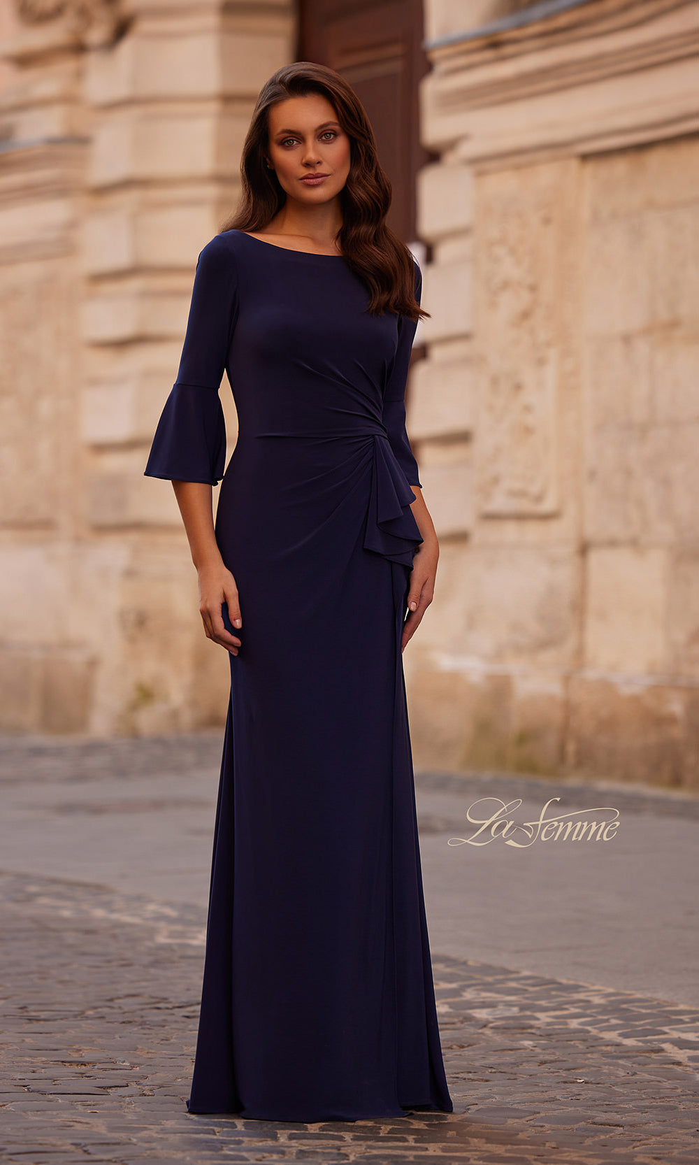 Woman wearing a navy blue evening gown with a brand name on a stone pavement background