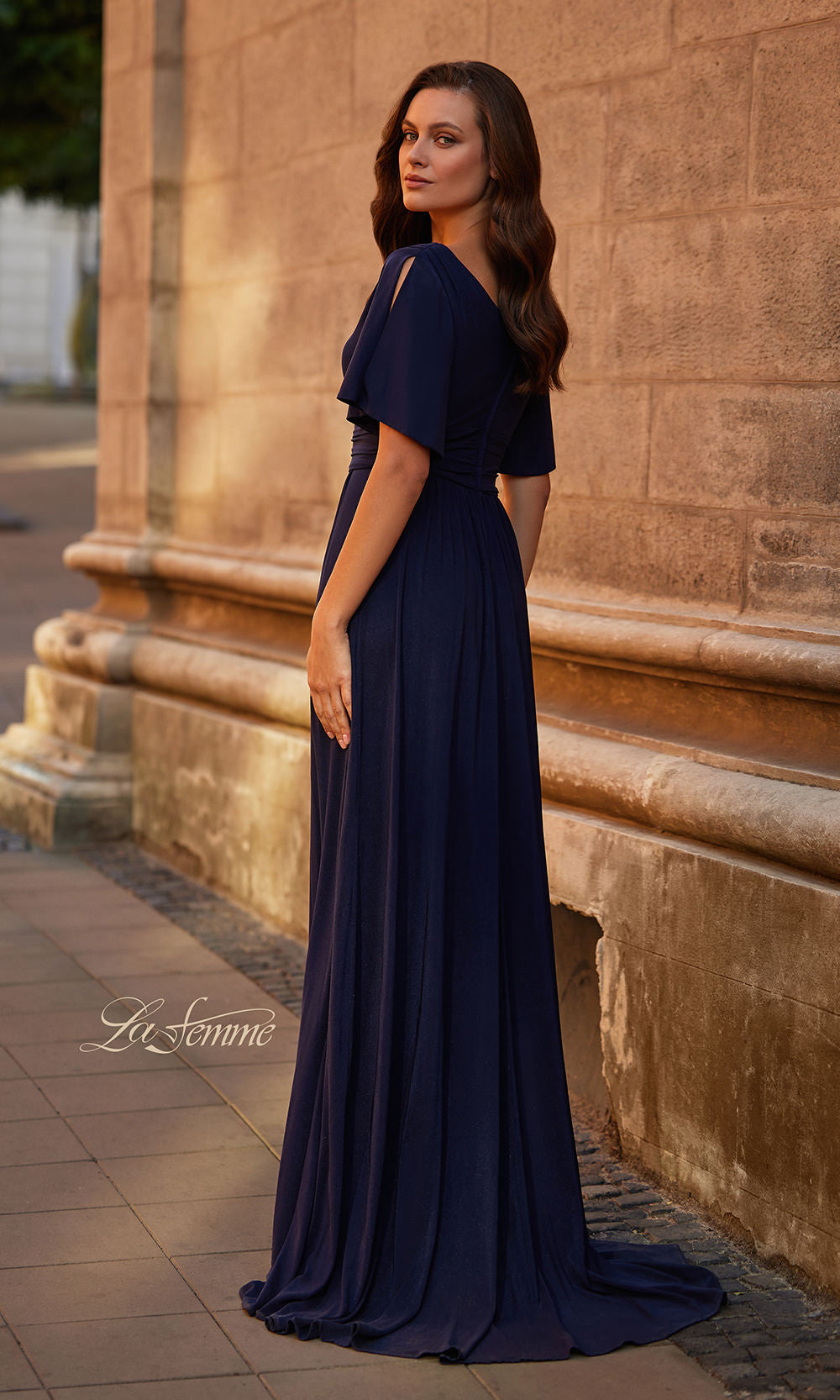 Woman in a navy blue evening gown standing against a stone wall.