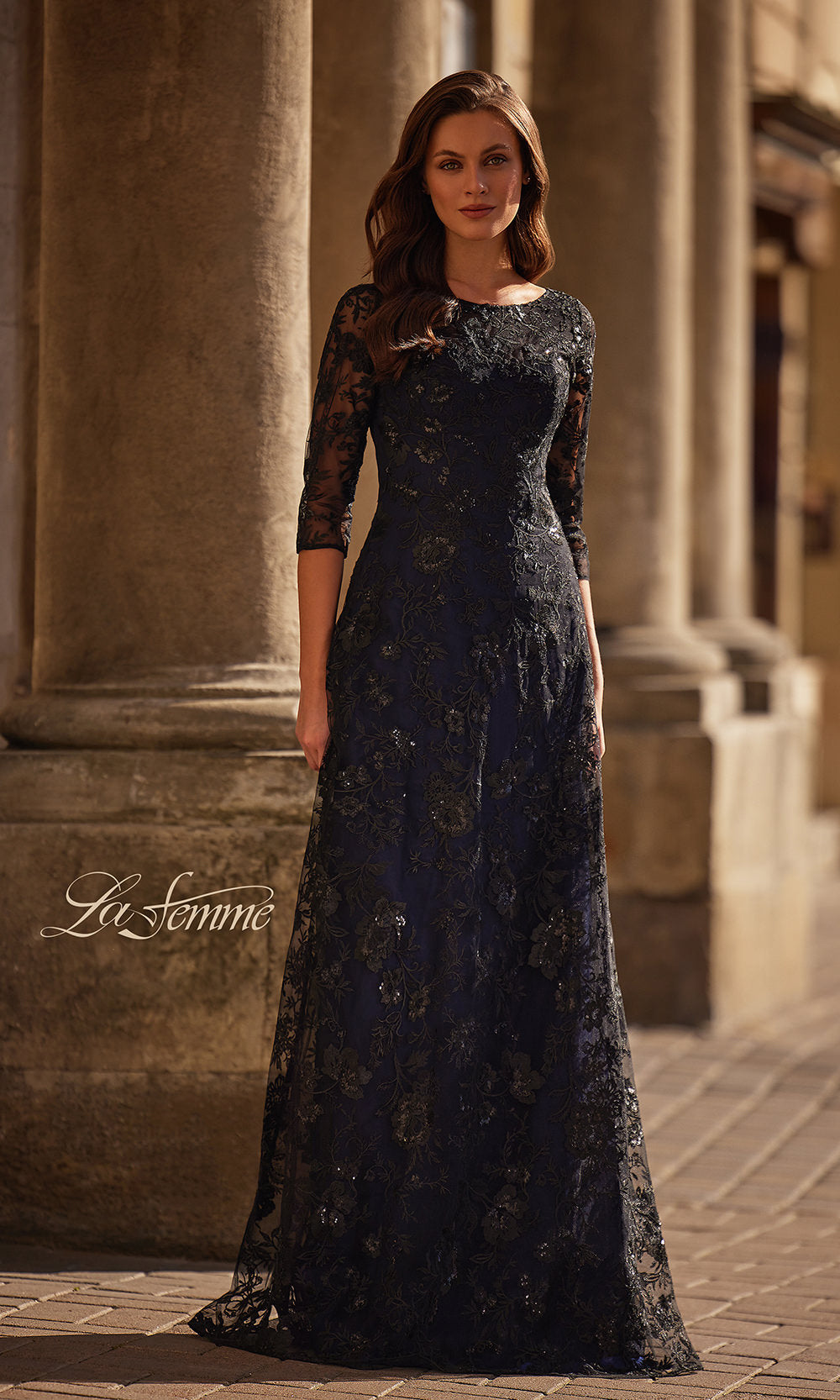 Woman wearing a dark lace evening gown standing in front of classical architecture.