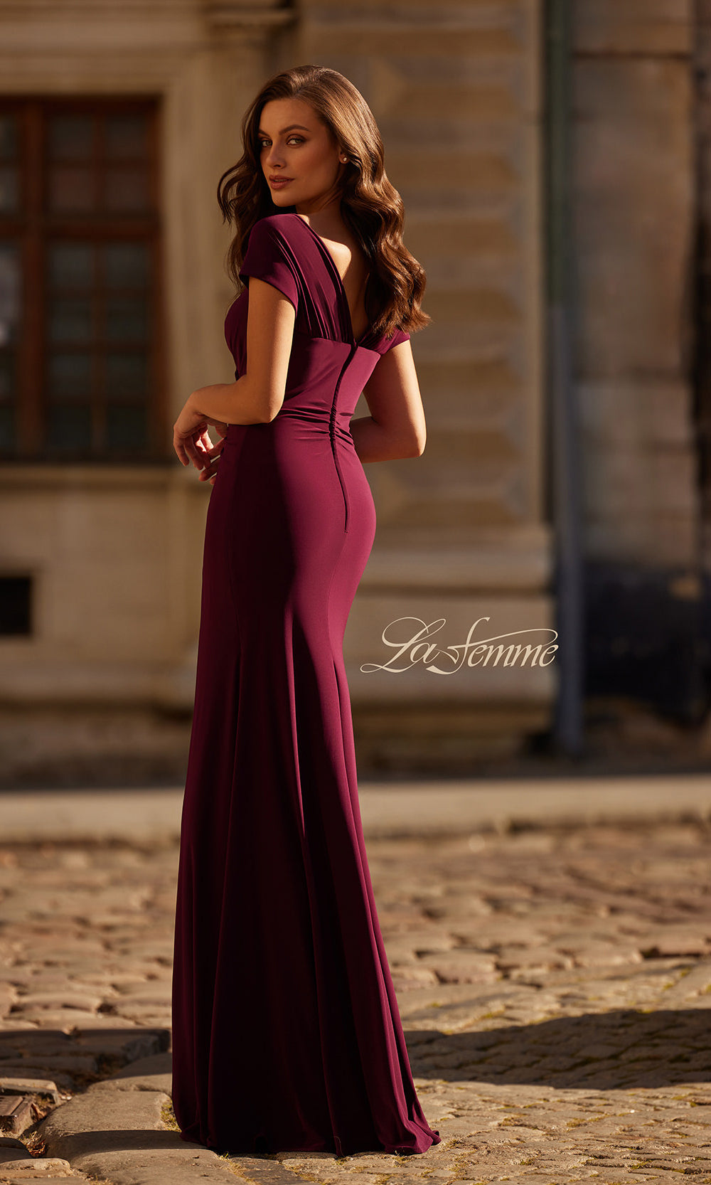 Woman in a long burgundy dress standing outdoors with 'La Femme' branding.