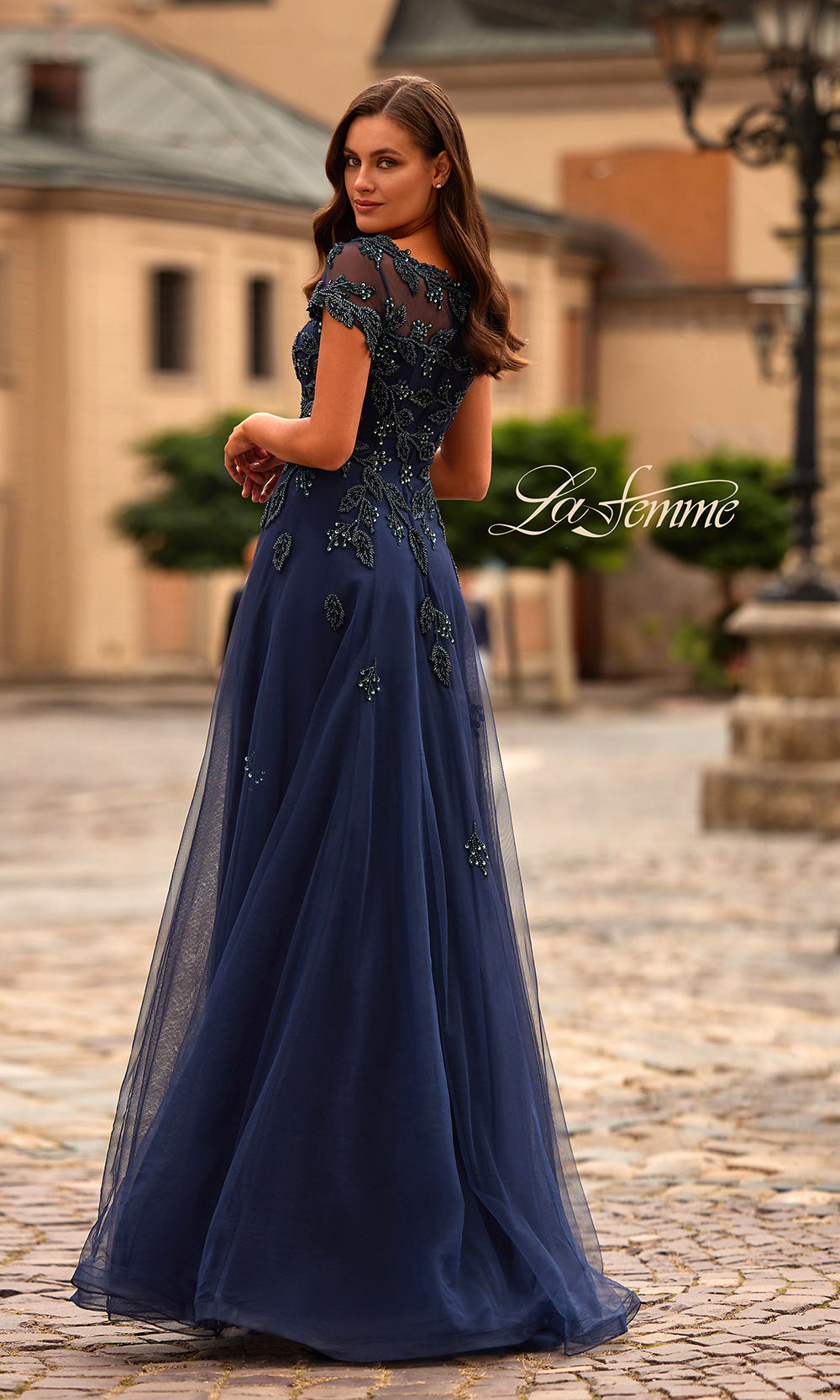 Woman wearing a navy blue evening gown with lace details on a cobblestone street.