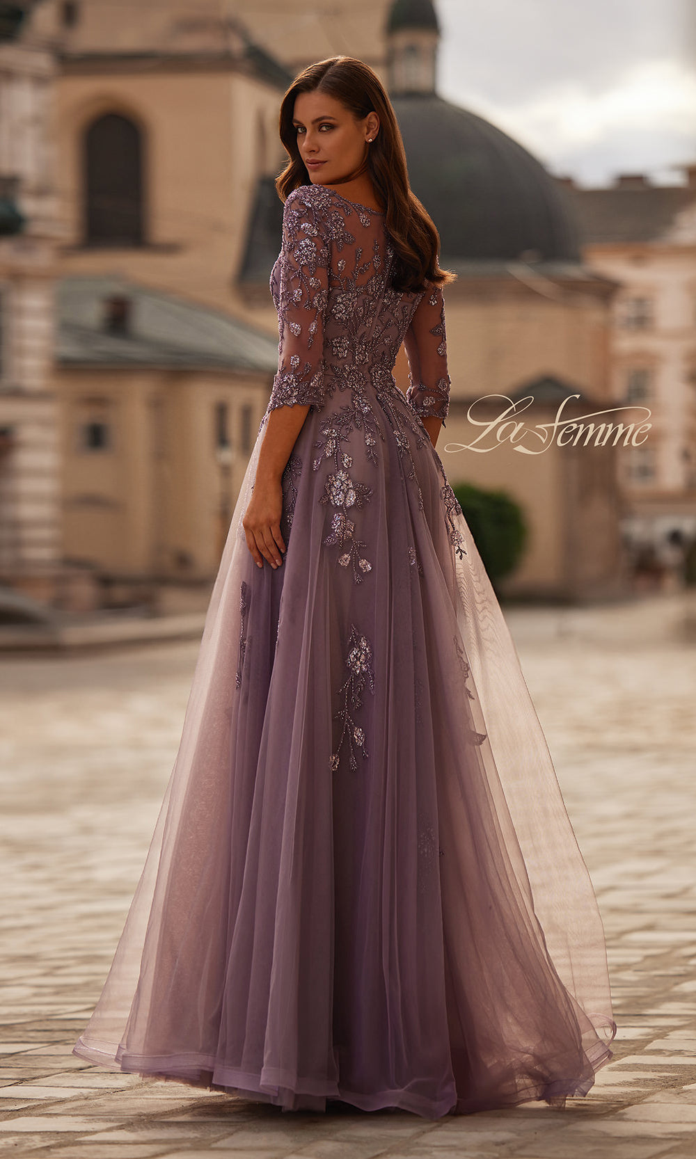 Woman in a purple evening gown with floral embellishments standing in an outdoor setting.