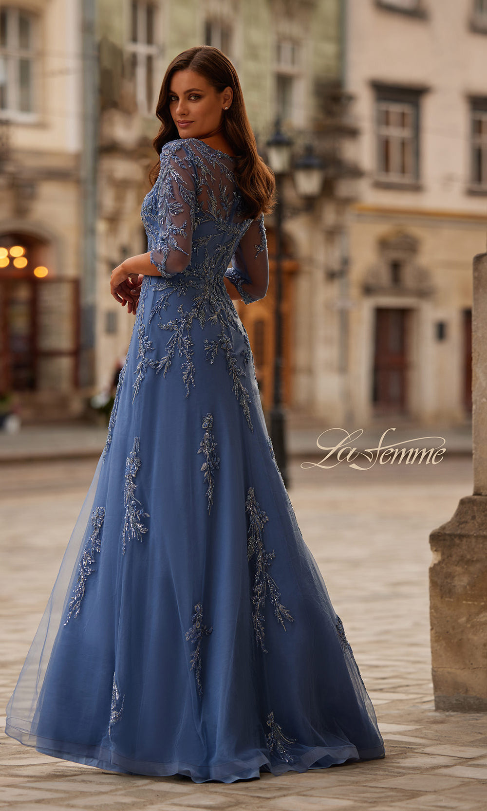 Woman wearing a blue evening gown with lace details in an urban setting.