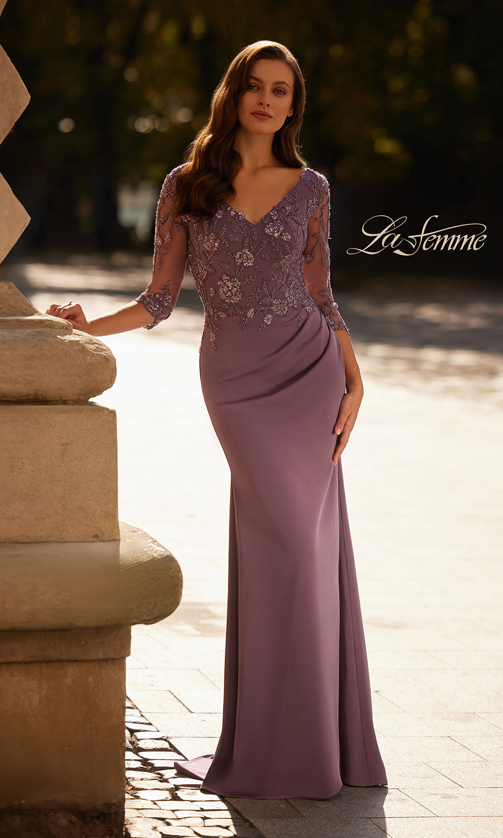 Woman wearing a long, elegant purple dress with floral lace details, standing outdoors.