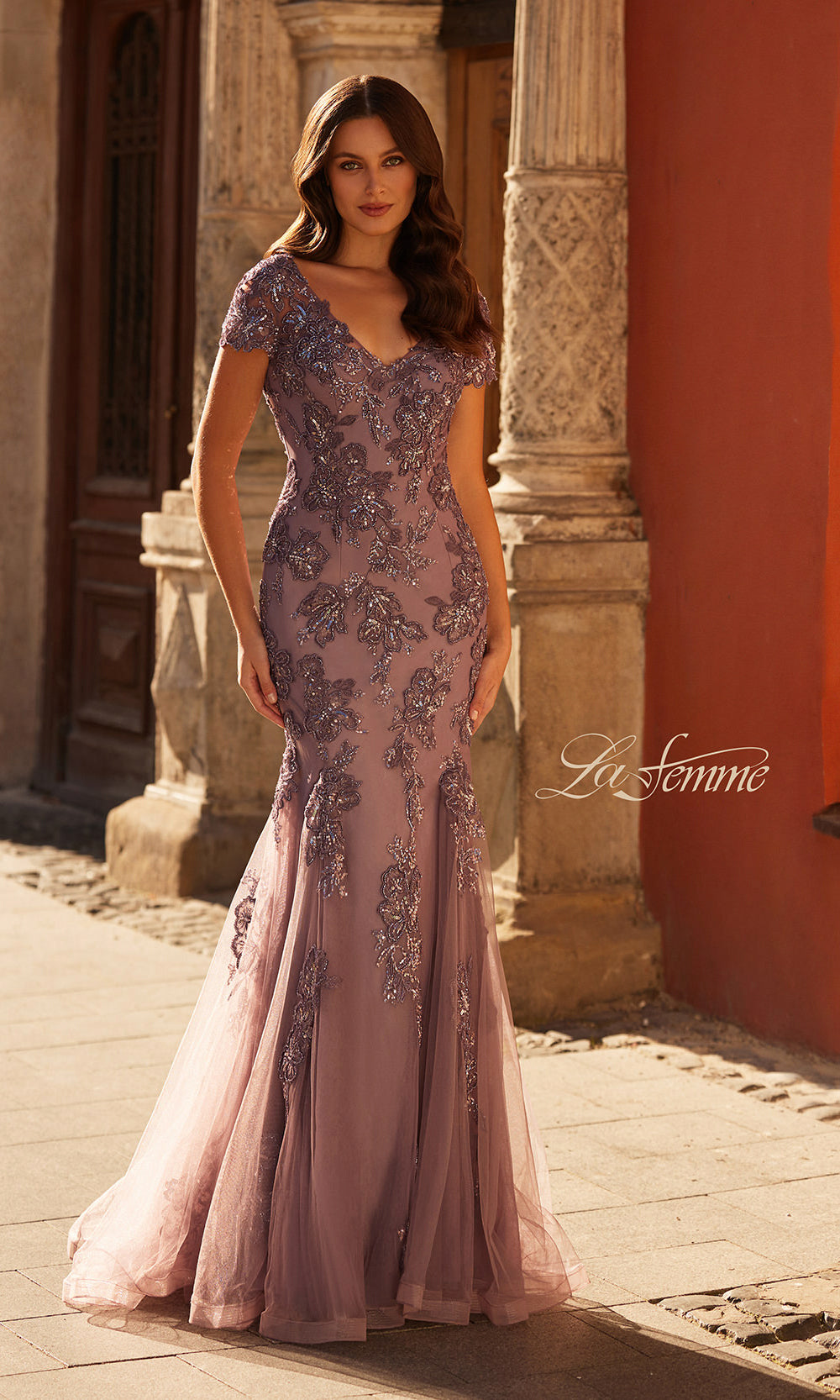 Woman wearing a pink evening gown with intricate detailing in an outdoor setting.
